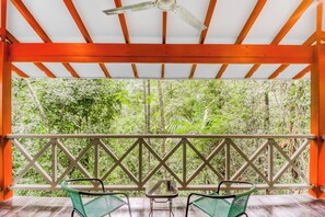 A covered outdoor seating area with two chairs and a table, overlooking a dense green forest.