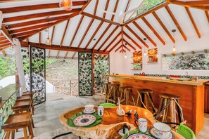Un intérieur rustique avec un plafond en bois, un coin bar et un espace repas comprenant des tabourets et une grande table.