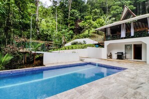 A swimming pool with a tiled edge, surrounded by a landscaped garden with various plants and trees.