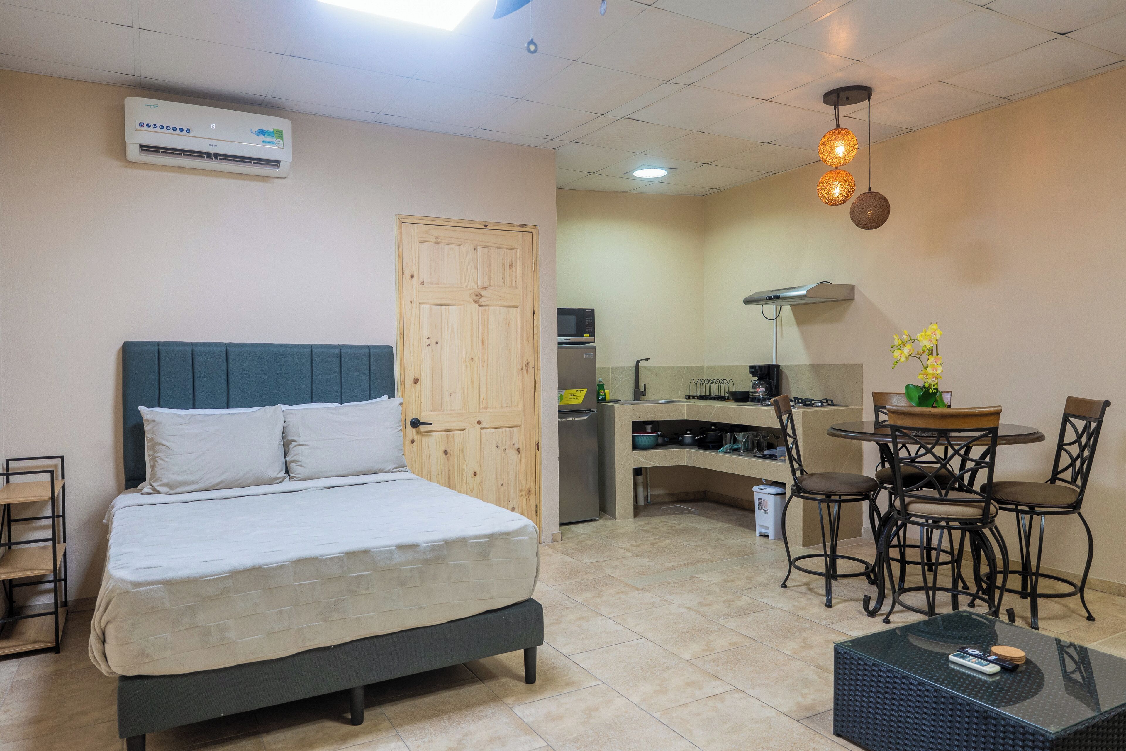 Een compacte hotelkamer met een bed, een kitchenette, een eethoek met stoelen en een tafel, en een plafondlamp.