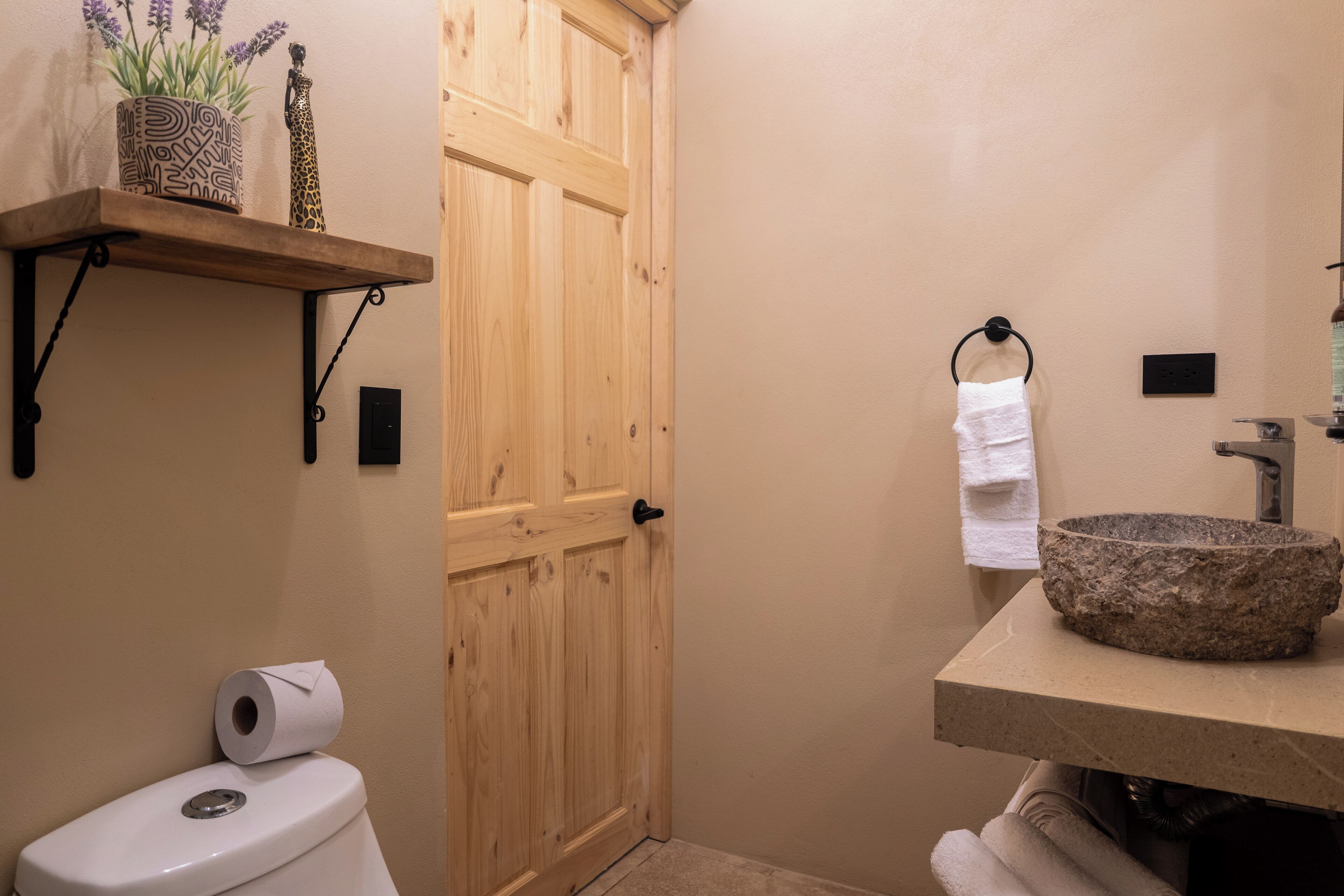 Ein Badezimmer mit Holztür, Toilette, Ablagefläche mit Dekoration, Handtuchhalter und Waschbecken aus Stein.