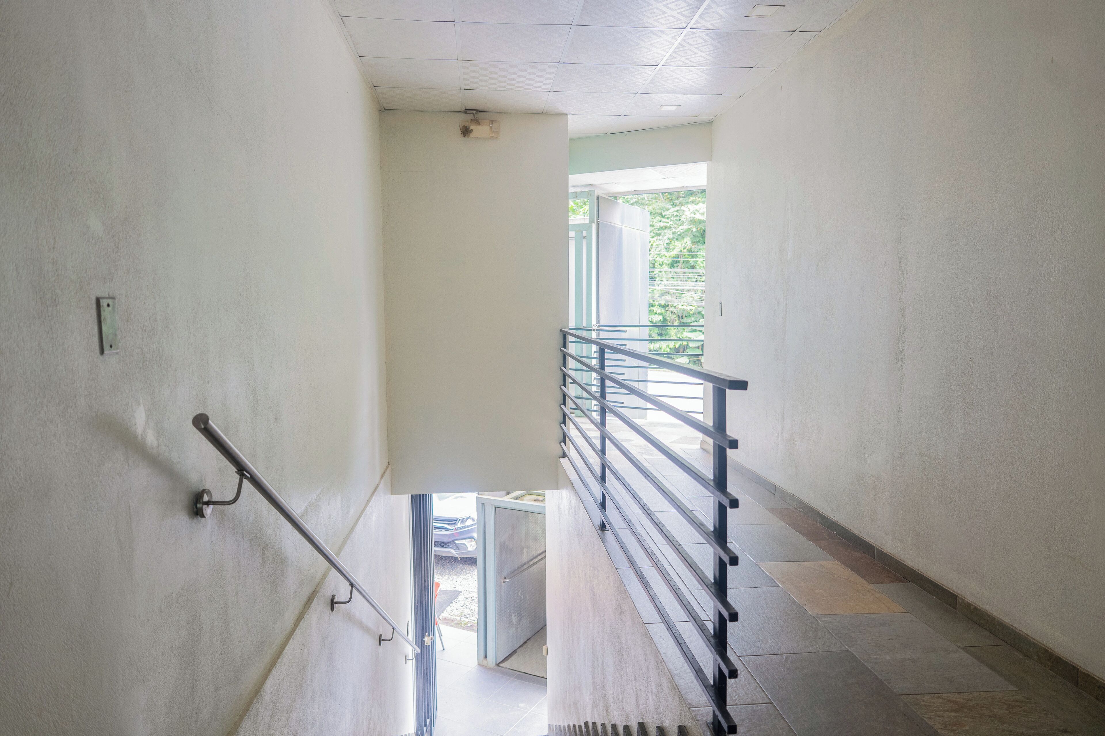A corridor with a handrail, a door leading to an outdoor area, and a staircase with a metal railing.