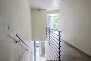Ein Korridor mit Handlauf, einer Tür zu einem Außenbereich und einer Treppe mit Metallgeländer.