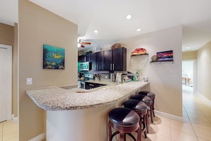 A kitchen with a granite countertop, dark cabinets, and a bar area with stools. - Playas del Coco: Balcony, Near Beaches! (Playas del Coco)
