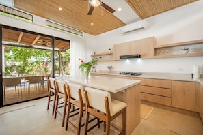 A modern kitchen with a central island, wooden cabinets, and a view of an outdoor pool area. - Modern Tamarindo Villa | Private Pool & Garden (Tamarindo)