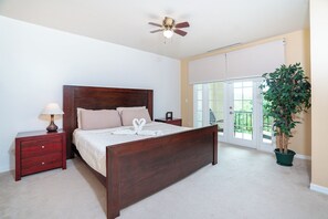Een slaapkamer met een houten bed, een nachtkastje, een lamp, een plafondventilator, een potplant en een schuifdeur naar een balkon.