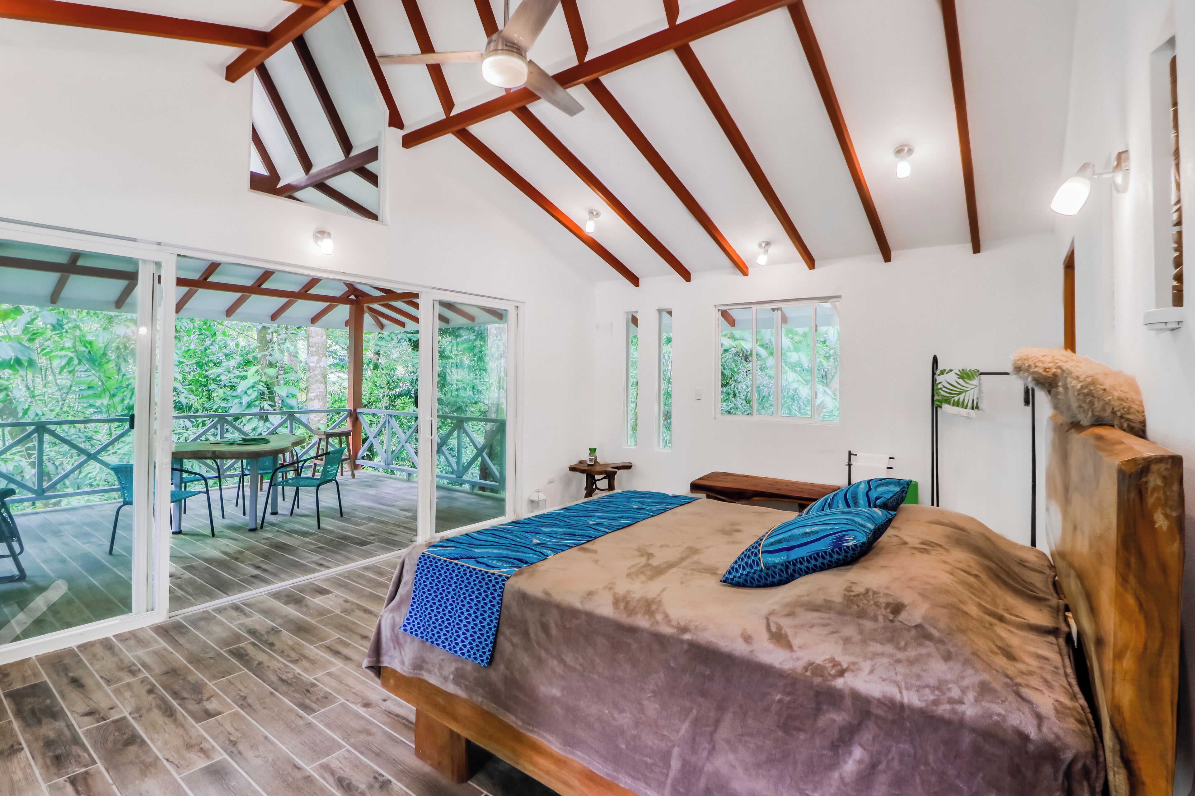 A bedroom with a large bed, a ceiling fan, and a view of greenery outside.