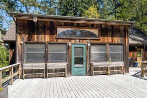Un edificio rústico de madera con puerta verde, ventanas amplias y una terraza de madera.