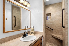 Un baño con un espejo grande, un lavamanos, una ducha y un perchero para toallas.