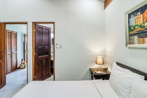 Ein Hotelzimmer mit einem Bett, einem Nachttisch mit Lampe, einem Bild an der Wand und einer Tür zu einem weiteren Raum.