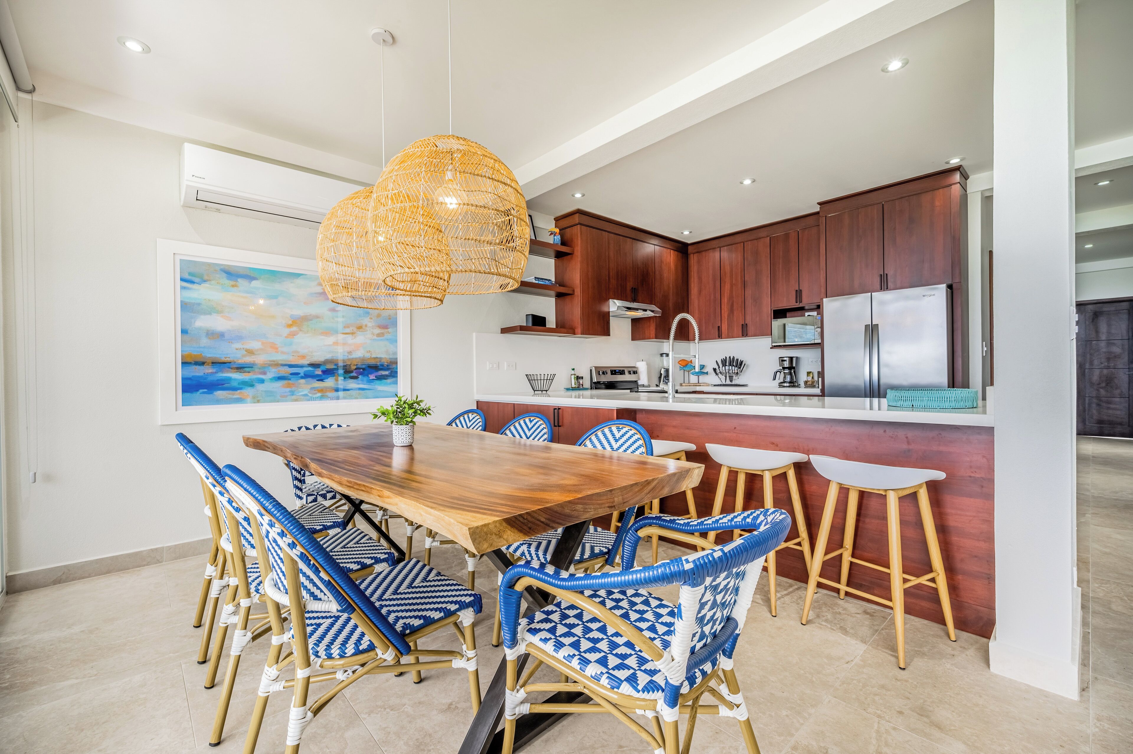 Une cuisine moderne avec une table à manger en bois, des chaises en osier et un luminaire suspendu.