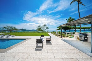 A poolside area with a view of the sea, outdoor seating, and a barbecue grill. - Playa Potrero: 2 Balconies & Private Grill (Playa Potrero)