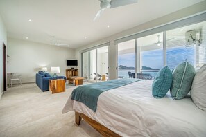 A bedroom with a large bed, a sofa, a TV, and a view of the sea. - Playa Potrero: 2 Balconies & Private Grill (Playa Potrero)