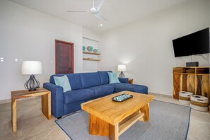 A living room with a sofa, coffee table, lamp, and a TV mounted on the wall. - Oceanfront Escape in Playa Potrero, Costa Rica (Playa Potrero)