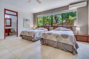 A hotel room with two beds, a large window with a view of trees, a bathroom with a mirror, and a ceiling fan. - Potrero Beachfront: Ocean-View Patio, W/D! (Playa Penca)
