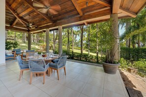 A covered outdoor dining area with a table set for four, surrounded by wicker chairs, under a wooden ceiling with a fan. - Potrero Beachfront: Ocean-View Patio, W/D! (Playa Penca)