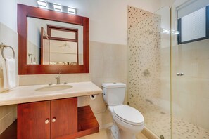 A bathroom with a wooden vanity, a toilet, and a glass shower enclosure. - Potrero Beachfront: Ocean-View Patio, W/D! (Playa Penca)