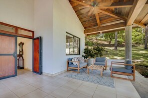 A spacious living area with a high ceiling, a wooden ceiling fan, and a view of a lush garden. - Potrero Beachfront: Ocean-View Patio, W/D! (Playa Penca)