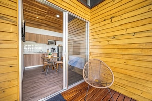 A wooden interior with a sliding glass door leading to a kitchen area, a dining table with chairs, and a wicker chair outside. - 2 Studios w/ Pool Access < 1 Mi to Playas Del Coco (Playas del Coco)
