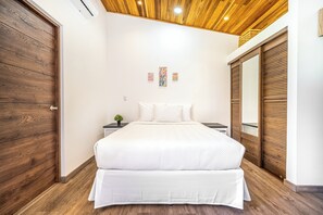 Ein Schlafzimmer mit Holzboden, einem Bett mit weißer Bettwäsche, einem Nachttisch mit Pflanze und einem Kleiderschrank mit Holzhörnern.