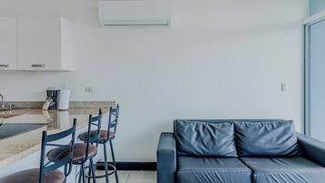 A modern living space with a kitchen area, a dining table with chairs, and a sofa with cushions.