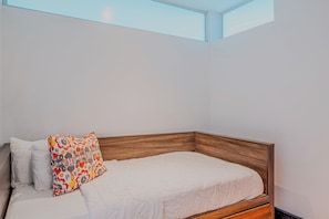 A bedroom with a wooden headboard, a white bedspread, and a colorful pillow.