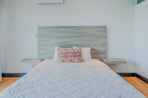 A neatly made bed with a white quilt, a wooden headboard, and two pillows with a colorful pattern.