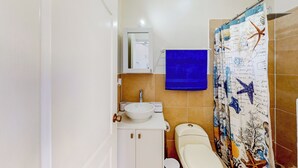Casa de banho com lavatório branco, espelho, sanita e cortina de chuveiro com tema náutico.