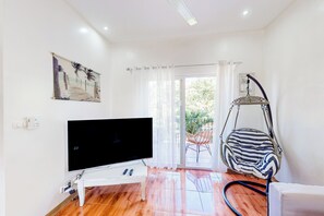 A modern living room with a flat-screen TV, a white coffee table, a hanging chair, and a view of the outdoors through a glass door. - Walk to Tamarindo Beach! Condo w/ 2 Balconies (Tamarindo)
