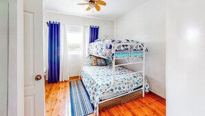 Uma cama de solteiro com edredom estampado, um ventilador de teto e uma janela com cortinas.