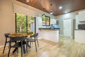 A modern kitchen with a central island, a dining area with a wooden table and chairs, and a view of the outdoors through a large window. - Shared Pool Access: Updated Apt in Playa Avellanas (Playa Avellanas)