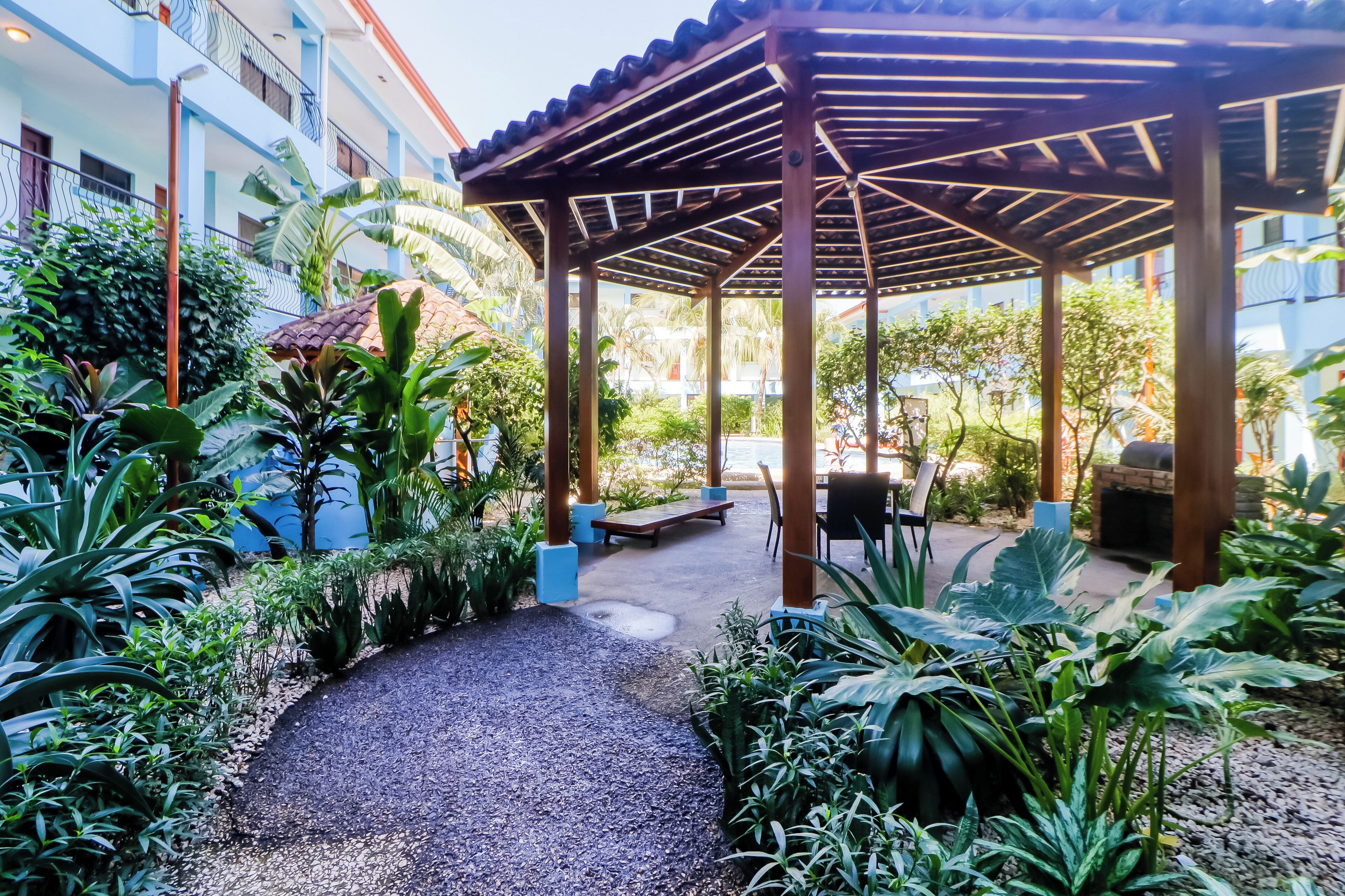 A covered outdoor area with a gravel path, seating, and lush greenery.
