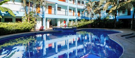 A hotel with a swimming pool, multiple balconies, and palm trees.