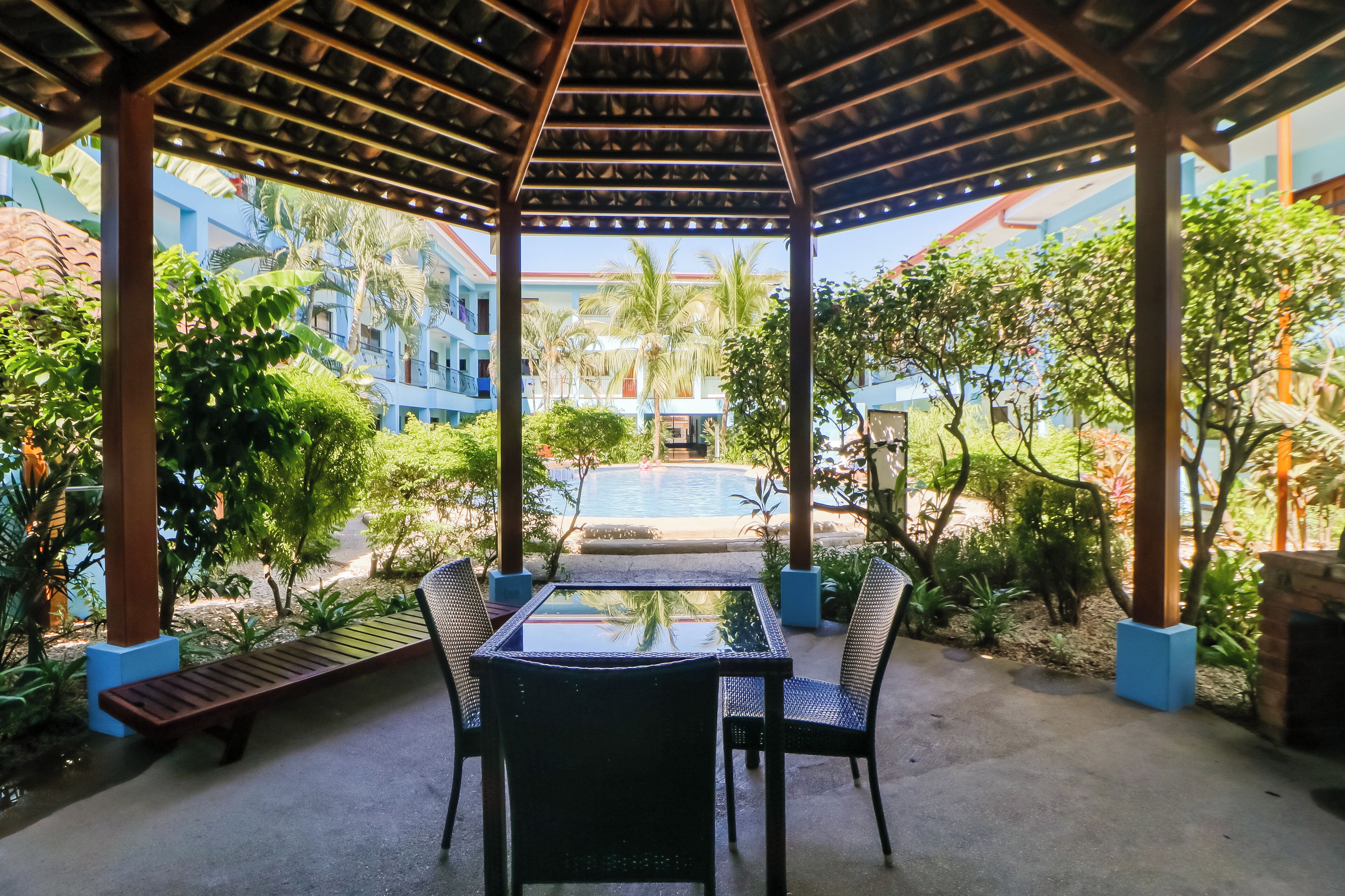 A covered outdoor seating area with a pool in the background.
