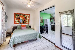 Une chambre à coucher avec un lit, un ventilateur de plafond, un tableau et une vue sur la cuisine.