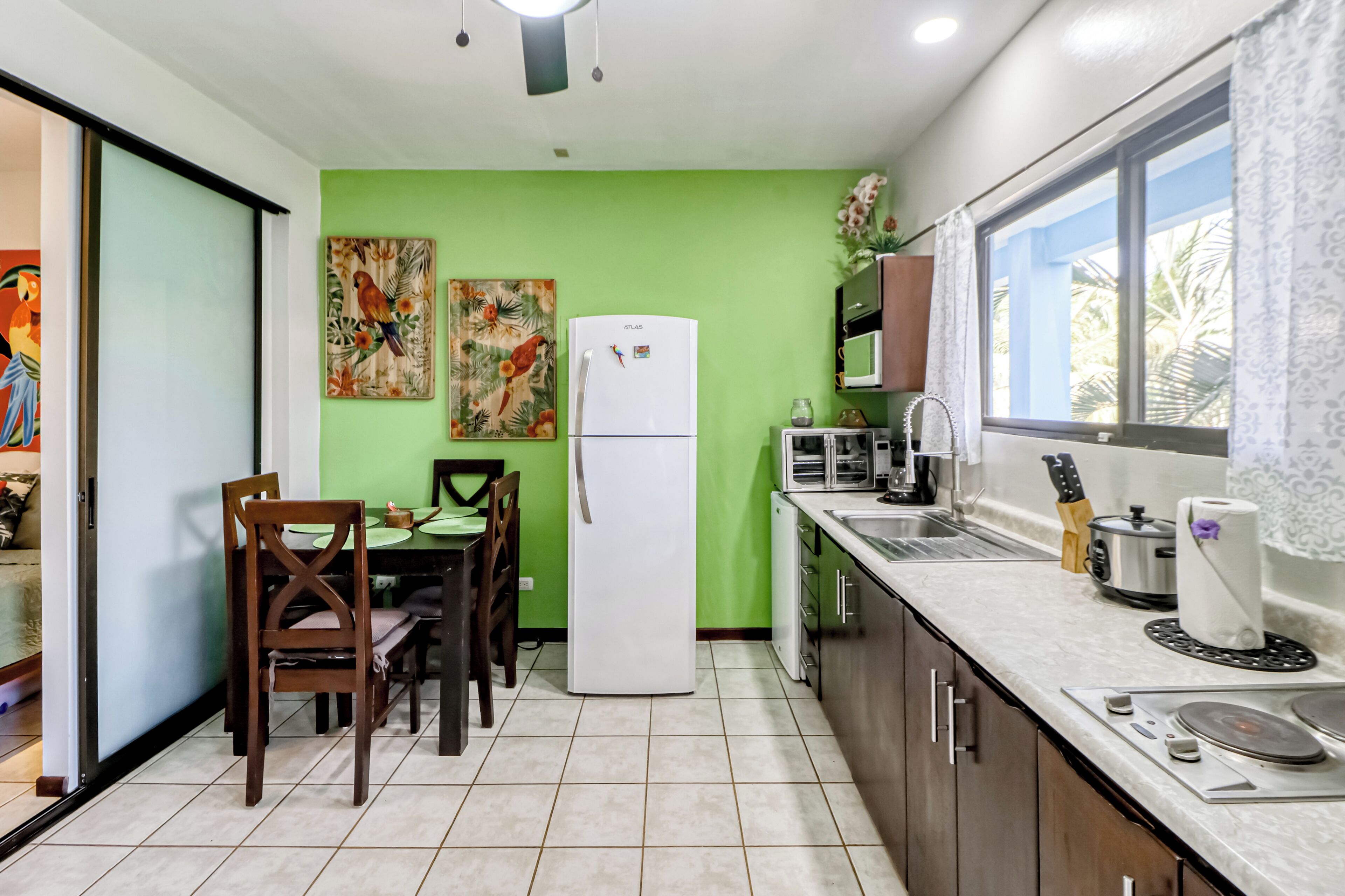 A compact kitchen with a refrigerator, microwave, and sink. There is a dining table with chairs and two wall-mounted paintings.