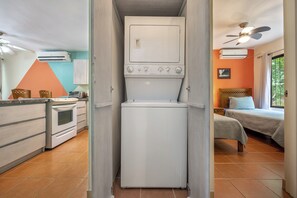 A compact kitchen with a built-in washer and dryer, a dining area with chairs, and a bedroom with a bed and a window. - Resort-Style Pool: Playa Ocotal Condo Near Beach! (Playa Ocotal)