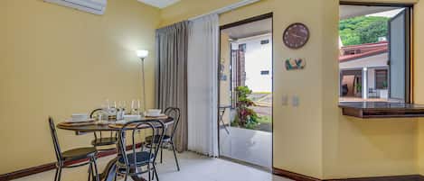 A dining area with a table set for four, chairs, a clock, and a view through an open door.