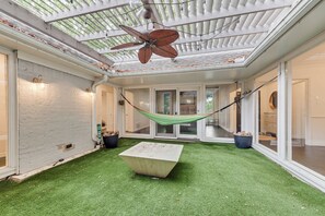Ein überdachter Patio-Bereich mit Kunstgrasanlage, einer Hängematte und einem Deckenventilator.