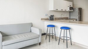 A compact kitchen with a white countertop, a built-in microwave, a stainless steel refrigerator, and a grey sofa.
