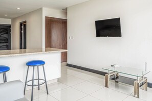 A modern kitchen with a bar area, a flat-screen TV mounted on the wall, and a glass coffee table.