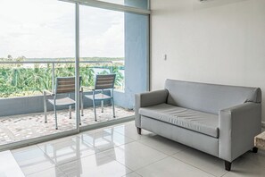 Een balkon met een bank en twee stoelen, een betegelde vloer en uitzicht op palmbomen en water.