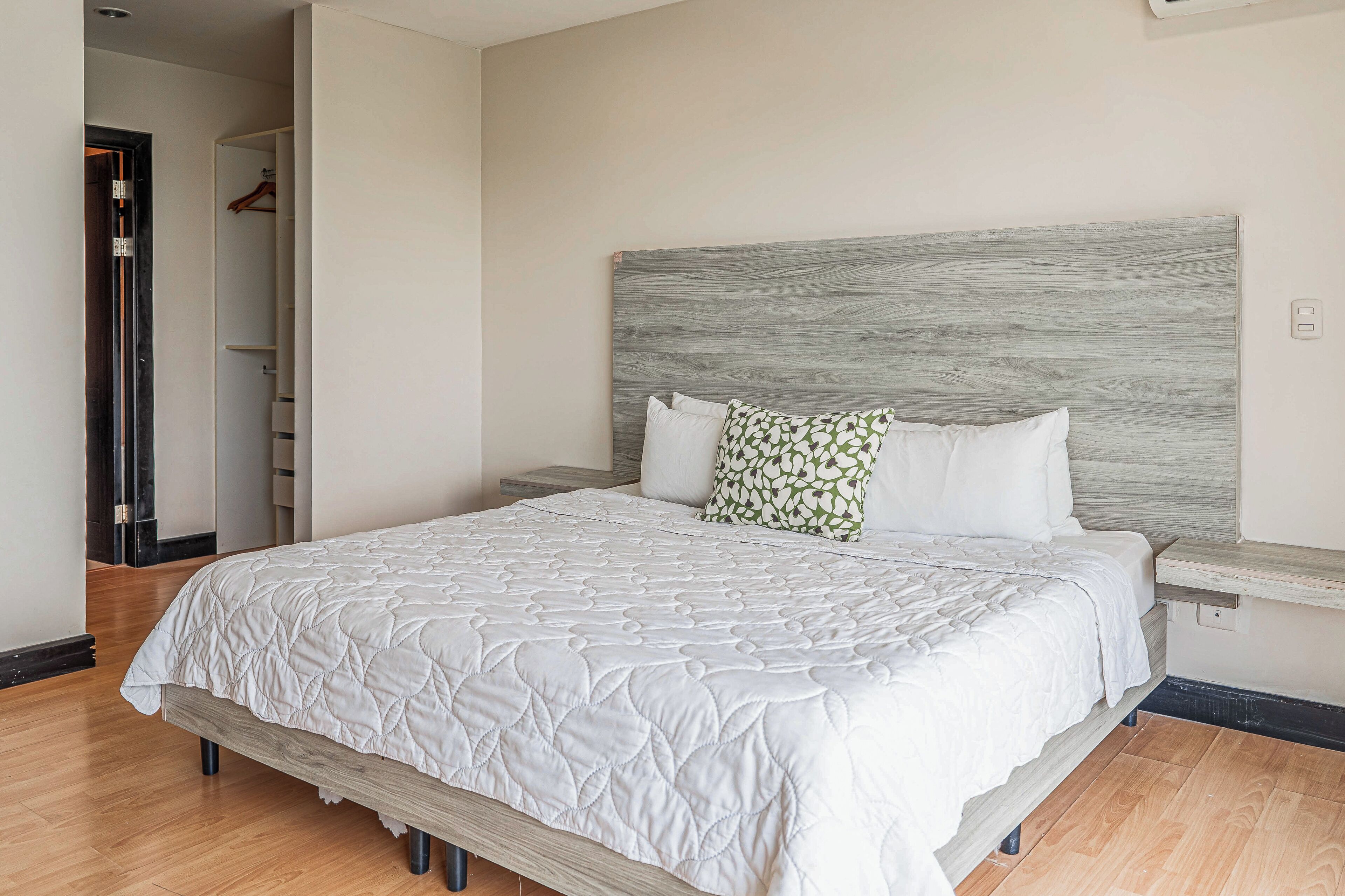 A neatly made bed with a quilted white bedspread, a wooden headboard, and two pillows, one plain and one with a leaf pattern.