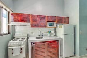 A compact kitchen with a stove, microwave, and refrigerator, wooden cabinets, and a window. - Playas del Coco Condo: Walk to Beach & Restaurants (Playas del Coco)