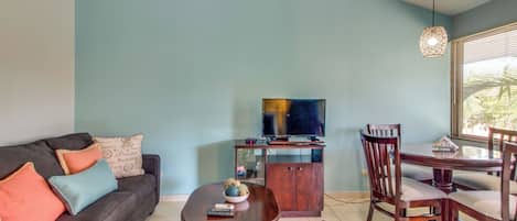 Ein Wohnzimmer mit Sofa, einem Esstisch mit Stühlen, einem Fernseher auf einem Schrank und einem Deckenventilator.
