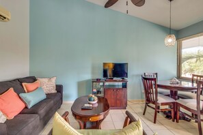 Ein Wohnzimmer mit Sofa, einem Esstisch mit Stühlen, einem Fernseher auf einem Schrank und einem Deckenventilator.
