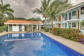 A swimming pool with a tiled deck, surrounded by palm trees and a building with balconies. - Playas del Coco Condo: Walk to Beach & Restaurants (Playas del Coco)
