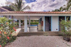 A covered outdoor area with a pool, palm trees, and a building with blue-framed windows. - Playas del Coco Condo: Walk to Beach & Restaurants (Playas del Coco)