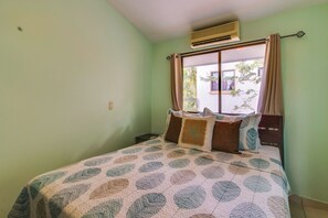 A bedroom with a bed, a window with curtains, an air conditioning unit, and a small bedside table. - Playas del Coco Condo: Walk to Beach & Restaurants (Playas del Coco)