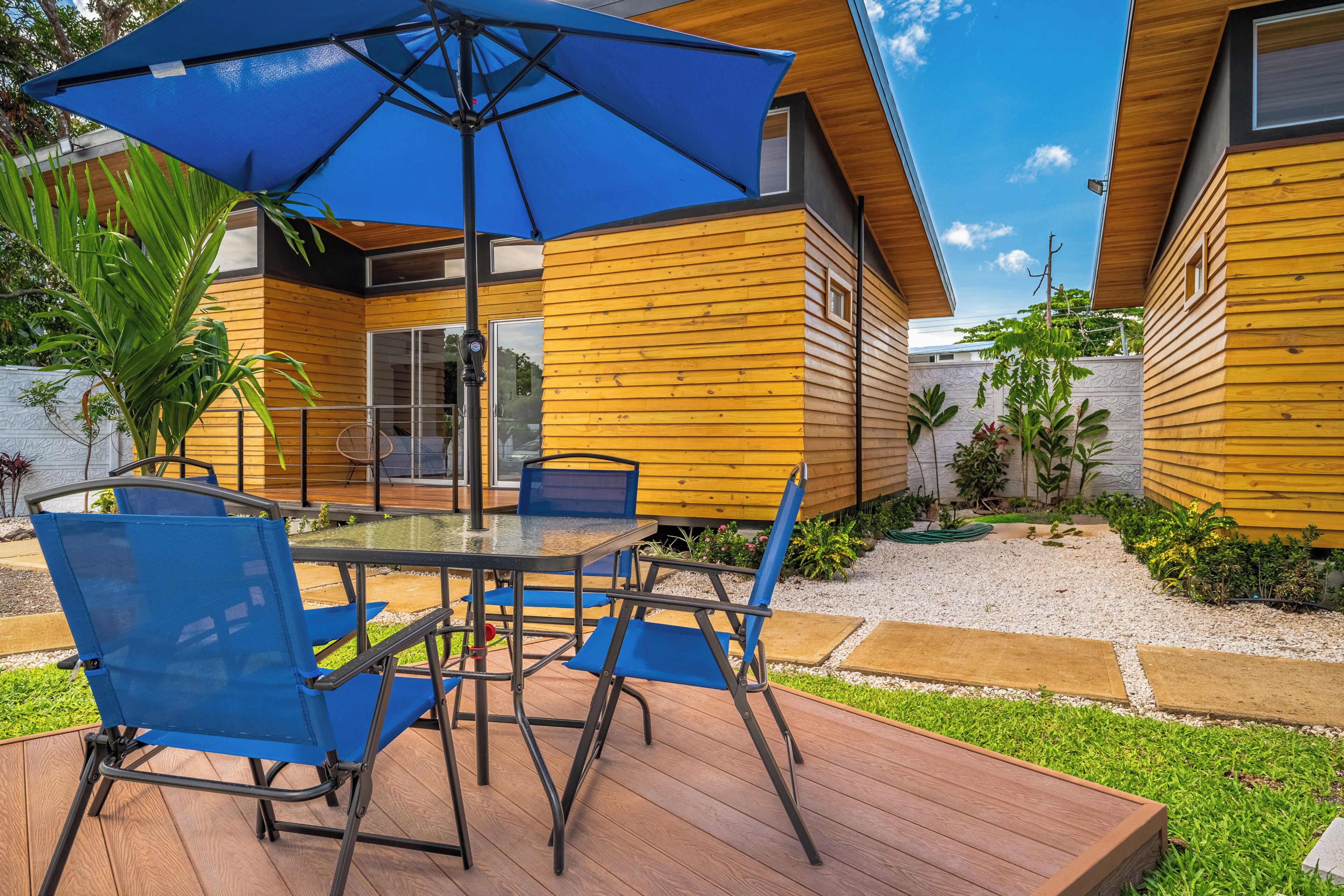 A deck with a table and chairs, an umbrella, and a wooden house with a window.